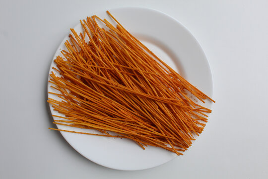 Mie lidi pedas, traditional snack from Indonesia. Noodle-like texture, fried and coated with chili powder. On white plate, isolated on white background, flat lay or top view