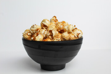 Caramel popcorn, in a black bowl, isolated on white background