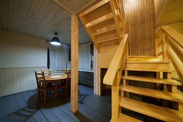 Interior of wooden house, kitchen with table and chairs, stairs to second floor