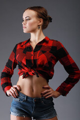 Young beautiful woman in red checkered shirt looks away in grey studio - obrazy, fototapety, plakaty