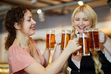 Two smiling women clang glass mugs with beer