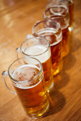 Several glass mugs of beer on wooden table, shallow dof