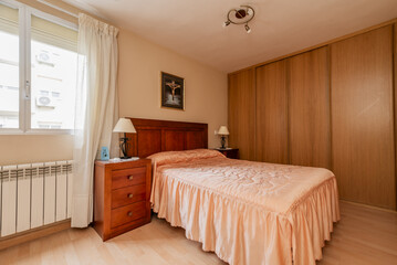 A double bedroom with wooden furniture, a large closet stuck to the wall and an ugly quilt on the bed