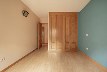 An empty bedroom with cream and green walls with a four-section built-in wardrobe with light wooden doors