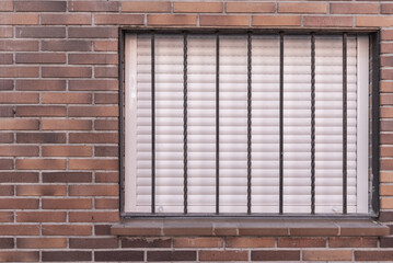 A brick wall with a window with the blinds down and a metal security gate