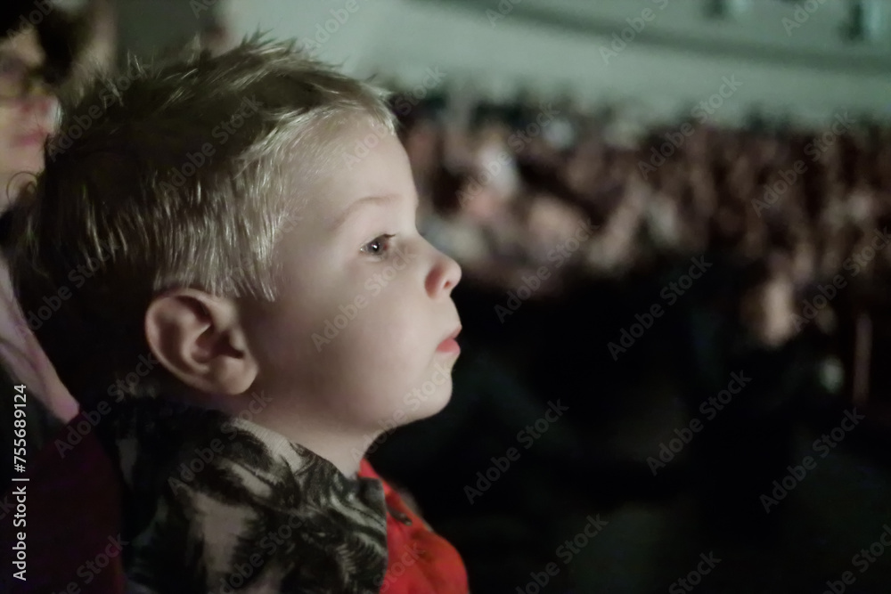 Wall mural Little cute boy looks at performance in big theater during show