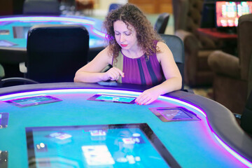 Pretty curly smiling woman sits at electronic poker table in casino, shallow dof