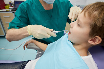 Dentist examines mouth and teeth of boy sitting in armchair