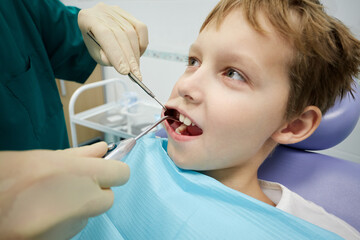Closeup dentist examines mouth and teeth of boy sitting in armchair