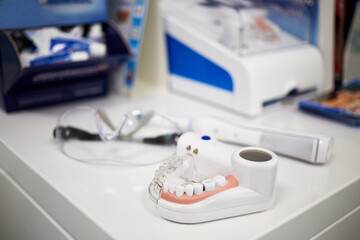 Fototapeta na wymiar Model of human jaw with teeth, electrical toothbrush and glasses on table, shallow dof