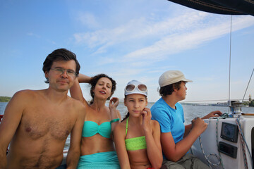 Mother, father, daughter and son sail on yacht on river at summer day