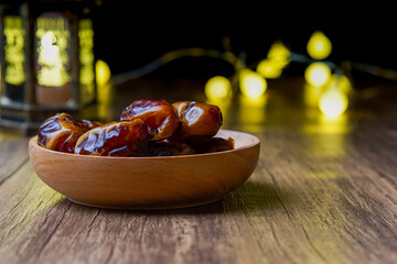 a close-up photo of dried dates served on a wooden bowl and a lantern with Arabic calligraphy...