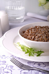 Cooked buckwheat lies in a white plate on a served table, vertical image