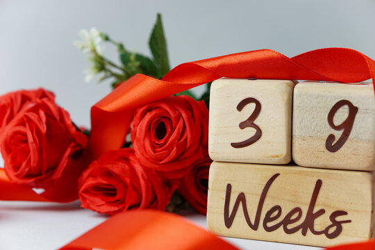 39 week gestational age milestone written on a wooden cube with red roses and ribbons, and a white background