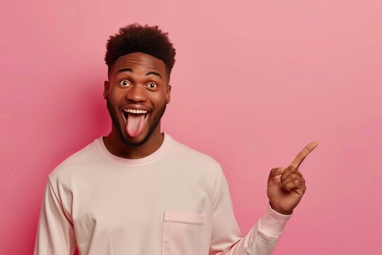 Photo of happy cheerful black male model points index finger aside, keeps mouth opened, shows tongue, attracts your attention to blank space, invites you going there, recommends product 