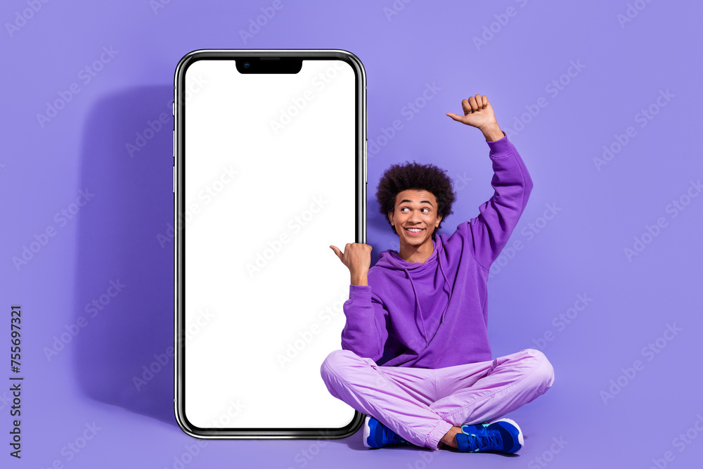 Poster Full length photo of satisfied guy sit near smartphone screen interested directing look empty space isolated on purple color background