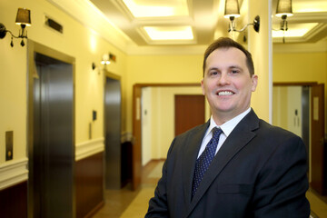 Portrait of smiling concierge in a business suit standing in the hallway between the elevator and...
