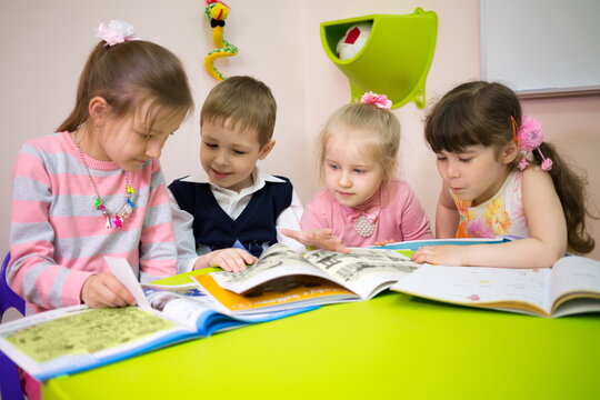 Four beautiful children are reading books at the table