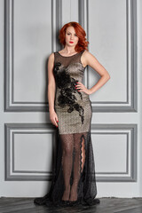 Red-haired young woman in white and black suit stands against door in room