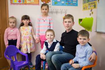Three boys are sitting on the arm-chair and three girls are standing near the wall