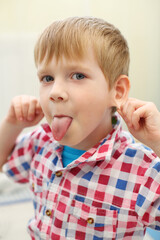 Little handsome blonde boy in checkered shirt grimaces, shallow dof