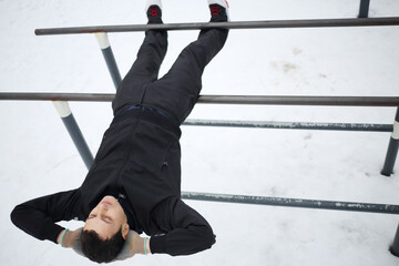 Man does exercises on parallel bars on sport playground in yard at winter