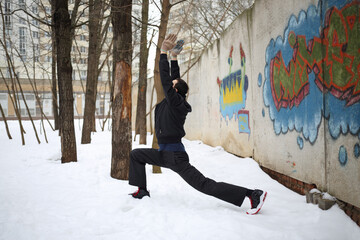 Man does exercises next to concrete wall with graffiti at winter