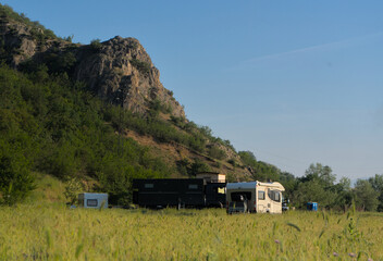 A camper park with campers at the foot of the mountains, steam rising from hot mineral springs visible. Bulgaria, Rupite