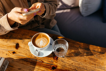 Girl holding a phone and taking picture of a cup of tea and a glass of water