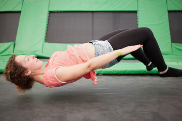 Young woman jumps on trampoline attraction in lying position - obrazy, fototapety, plakaty