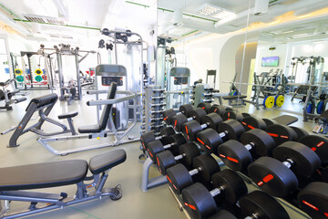 Fototapeta na wymiar Modern gym with new shiny fitness equipment, big mirror, dumbbell set for sport training