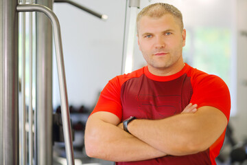 Young strong man stands with arms crossed in modern gym with fitness equipment