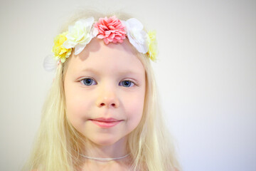 Little pretty blonde girl in wreath smiles in room with white wall