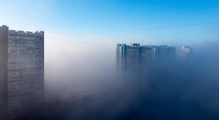 A white-and-blue multi-storey residential building is shrouded in fog in the early spring morning.