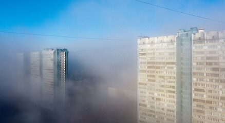 A white-and-blue multi-storey residential building is shrouded in fog in the early spring morning.