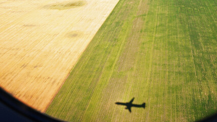 View through the airplane window of its own shadow on the background of a field; travel the world concept