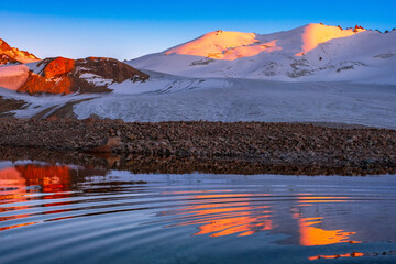 Mountain peaks reflected in an icy lake at sunset; wonderful mountain landscape in the soft light of the setting sun