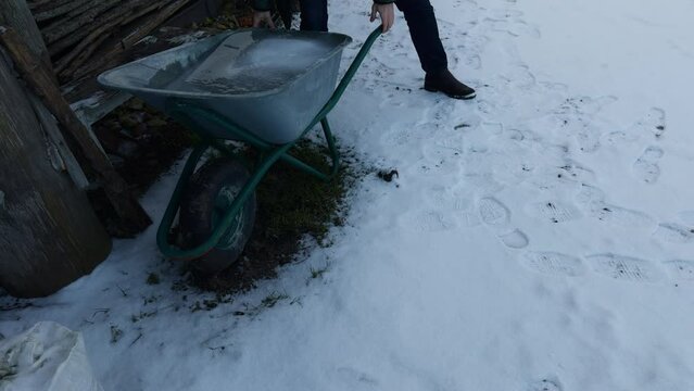 Man turns over a wheelbarrow with huge ice block falling on the snow