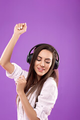 Gorgeous brunette lady  listening music in wireless headphones and singing on  purple background. Charming girl in wireless earphones dancing.