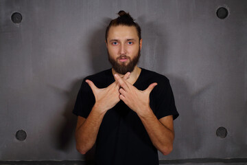 Fashionable handsome man with beard poses in studio near wall