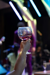 hand holding a glass of wine, glass of wine in nightclub, alcohol drink cup,cocktail, night party, dance floor

