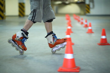 Legs of roller skater posing on floor near orange cones in indoor parking