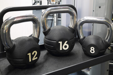 Three modern black kettlebells are on table in fitness center
