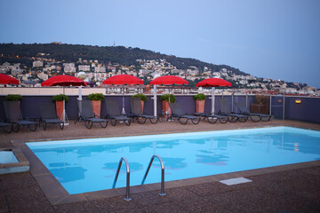 Fototapeta na wymiar Empty small pool on rooftop, loungers, umbrellas at evening in town on mountain