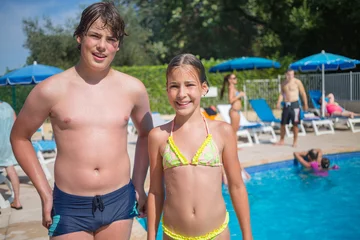 Gordijnen Smiling boy and girl in swimsuit pose near outdoor pool at sunny day, other people out of focus © Pavel Losevsky