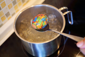  Hand gets out of boiling water egg with cover with print in kitchen. There is tradition to put pictures on eggs in Orthodox Easter in Russia