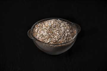 Rye flour in glass bowl on black background.