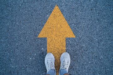 Runner standing on asphalt road with yellow arrow for go ahead and never give up to running , it will use in conceptual of business , lifestyle.