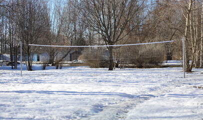 A white volleyball net is stretched over a snow-covered volleyball court