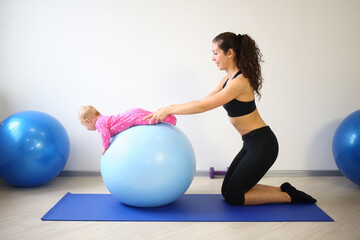 Fototapeta na wymiar Mother and baby doing exercises on the big blue ball in the gym